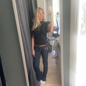 Svart topp med volangdetaljer - Snygg svart topp med volangdetaljer på axlarna. Perfekt för en stilren look. Toppen är ärmlös och har en normal passform.