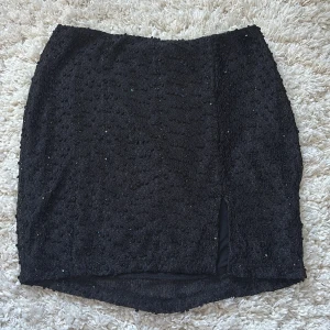 Svart glittrig kjol med slits - Snygg svart minikjol med glittrande detaljer och en liten slits framtill. Kjolen har en dragkedja på sidan. Från NA-KD, aldrig använd ✨ 