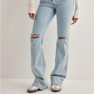 Lågmidjade bootcut jeans ifrån Nelly - Snygga ljusblå bootcut jeans med slitningar på knäna och coola broderade detaljer på bakfickorna. Perfekta för en avslappnad stil med en touch av edge.