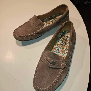 Bruna mockaloafers från Sebago - Snygga bruna loafers i mocka från Sebago med ett färgglatt blommigt mönster på insidan. Perfekta och bekväma, klassiska ”båtskor”. 🩷Säljer på grund av att de är för små för mig som har 38. Skriv för fler bilder!