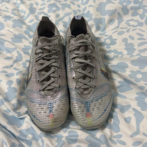 Nike mercurial elite vapor 16 - Snygga grå fotbollsskor från Nike med färgglada detaljer och snörning. Skorna har en modern design med en slitstark sula och dobbar i gult för bra grepp på planen. Perfekta för fotbollsspelare som vill ha stil och funktionalitet.