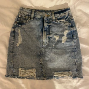 Blå jeanskjol  - Snygg blå jeanskjol från &Denim (H&M) med slitna detaljer och rå kant. Kjolen är knappast använd.