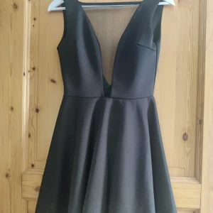 Svart klänning från Club L - Säljer en elegant svart klänning från Club L. Den har en djup v-ringning och är ärmlös, vilket gör den perfekt för festliga tillfällen. 