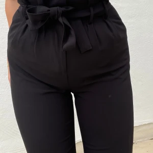 Svarta byxor med knytband - Säljer ett par snygga svarta byxor med hög midja och knytband i midjan. De är i en loose passform och har en stilren look som passar perfekt för både vardag och fest. Materialet känns mjukt och bekvämt.