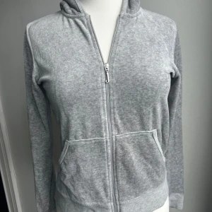 Grå hoodie från Juicy Couture - Säljer en supermjuk och bekväm grå hoodie från Juicy Couture. Den har en dragkedja framtill och en klassisk huva. Perfekt för en avslappnad stil eller mysiga dagar hemma. Den är i storlek M och i bra skick.
