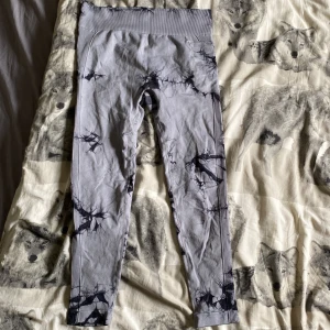 Grå leggings med mönster - Säljer ett par grå leggings med coolt svart mönster. De är gjorda av 92% polyamid och 8% elastan, vilket gör dem superstretchiga och bekväma. Perfekta för träning eller en chill dag hemma. De har en hög midja och ribbad detalj upptill för extra komfort.
