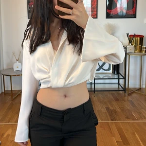 Vit omlottblus Zara - Säljer en superfin vit omlottblus med långa ärmar. Den är croppad och har en snygg v-ringad design som ger en stilren look. Perfekt för både fest och vardag!