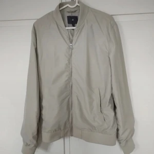 Beige bomberjacka från H&M - Säljer en stilren beige bomberjacka från H&M. Jackan har en dragkedja framtill och långa ärmar. Perfekt för vår och höst! 🧥