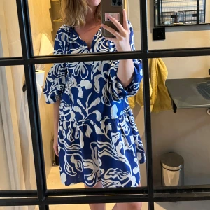 Blå och vit klänning från H&M - Säljer en superfin blå och vit klänning från H&M. Den har ett coolt abstrakt mönster och är perfekt för sommaren. Klänningen är kort och har resår längst ut i ärmen så att ärmarna kan dras upp. Perfekt för en dag på stan eller en sommarfest! 💙