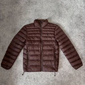 Polo Ralph Lauren dunjacka  - Unik dunjacka från Polo Ralph Lauren i färg Nutmeg Brown. Modellen heter Terra Jacket och nypris ligger på 4295kr. Storlek XS. Modellen i bilden är 1,83. Helt ny, oanvänd med tags kvar. Enbart testat.