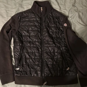 Svart quiltad jacka från Moncler - Säljer en snygg svart cardigan från Moncler. Den har en dragkedja framtill och två fickor med dragkedjor. Jackan är långärmad och har en ribbad krage och muddar. Perfekt för höst. Den e väldigt använd och lite defekt i dragkedjan, Skick 6/10