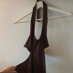 Brun ribbad klänning - Snygg brun ribbad klänning med djup urringning och breda axelband samt öppen rygg. Perfekt för en stilren look. Klänningen har en lång design som ger en elegant känsla.