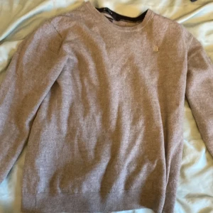 Beige tröja från Tiger of Sweden - Säljer en stilren beige tröja från Tiger of Sweden, tillverkad av fin italiensk garn. Tröjan har en diskret logga på bröstet och rund halsringning. Perfekt för en elegant och avslappnad look.