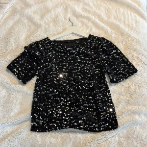Svart paljettopp - Glamorös svart topp täckt med glittrande paljetter. Perfekt för en festlig kväll eller slutet utav året. Toppen har korta ärmar och en rak passform som ger en stilren look.
