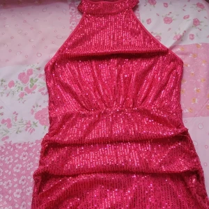 Rosa glittrig klänning - Snygg rosa klänning med glittriga paljetter som ger en festlig look. Klänningen har en tight passform och är ärmlös, perfekt för en utekväll. Den har en hög hals och en dragkedja i ryggen för enkel påklädning.