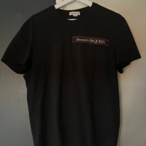 Svart t-shirt från Alexander McQueen - Snygg svart t-shirt från Alexander McQueen med logga på bröstet. Tillverkad i Portugal och perfekt för en stilren look. Passar bra till både jeans och shorts.