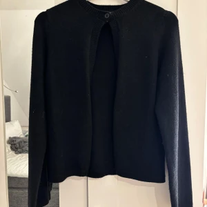 Svart kofta med knappdetalj - Säljer en stilren svart kofta med en enkel knappdetalj vid halsen. Koftan har långa ärmar och en klassisk design som passar till många olika outfits. Perfekt för kyligare dagar.