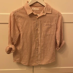 Randig skjorta från Zara - Säljer en snygg randig skjorta från Zara i storlek 152. Skjortan har en klassisk krage, knappar framtill och en bröstficka. Perfekt för en stilren look!