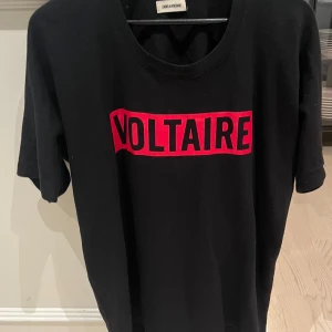 Svart t-shirt från Zadig & Voltaire - Snygg svart t-shirt från Zadig & Voltaire med röd text på bröstet. Perfekt för en casual look med en skön passform och korta ärmar. Den är stor i storlek men väldigt skön
