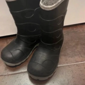 Svarta stövlar st 28 - Säljer ett par svarta stövlar med robust design. Perfekta för regniga dagar och leriga stigar. De har en hög skaft och en slitstark sula för extra grepp.