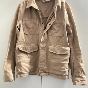 Beige manchesterjacka - Säljer en snygg beige overshirt med dragkedja och knappar. Jackan har två stora fickor framtill och en klassisk krage. Perfekt att ha över en go hoodie eller liknande fungerar bra både inne och ute. passar dig som är mellan 150-160|| Hör av dig vid minsta fundering eller fråga!!