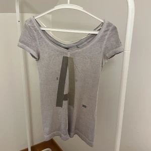 Grå t-shirt från G-Star RAW - Snygg grå t-shirt från G-Star RAW med ett stort tryck av bokstaven 'A' på framsidan. T-shirten har en v-ringad hals och korta ärmar, perfekt för en avslappnad stil.