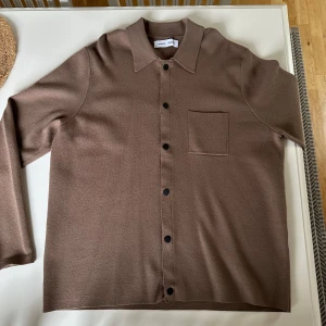 Brun kofta från Samsøe Samsøe - Snygg brun kofta från Samsøe Samsøe i en mjuk och bekväm design. Skjortan har långa ärmar och knappar framtill samt en praktisk bröstficka. Perfekt för en stilren look.