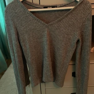 Grå ribbad tröja från BikBok - Säljer en stilren grå ribbad tröja från BikBok i storlek XS. Tröjan har en v-ringad design och långa ärmar, perfekt för en avslappnad look. Passar bra till både jeans och kjol. Perfekt för höst och vinter!