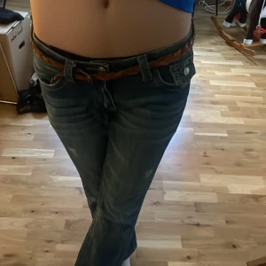 Blå jeans från True Religion - Snygga blå jeans från True Religion med broderade detaljer på bakfickorna och en flätad bälte. Jeansen har en klassisk femficksdesign och en knappgylf. Perfekta för en avslappnad stil. Väl använda. Mamma köpte dom för ca 15-20 år sedan för 2000kr. Idag ligger dem på 1299(nya) pris 700kr. Pris kan diskuteras💞