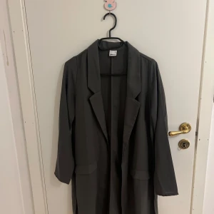 Grå kappa från Gina tricot - Mörkgrå kappa från Gina tricot, jättefin och oanvänd, slits på sidorna och den är perfekt inför sommarn.