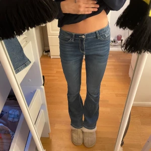 Blå bootcut jeans - Snygga blå bootcut jeans med låg midja och dekorativa sömmar på bakfickorna. Perfekta för en avslappnad stil. De har en klassisk femficksdesign och stängs med dragkedja och knapp.