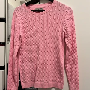 Rosa stickad tröja från basic you  - Säljer en snygg rosa stickad tröja från basic you. Tröjan har ett klassiskt flätmönster och långa ärmar. Perfekt för kyligare dagar och ger en stilren look. Passar bra till både jeans och kjol. 🌸