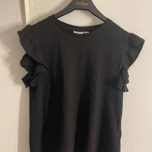 Svart topp med volangärmar från Gina!💗 - Säljer en stilren svart topp från Gina Tricot med volangdetaljer på ärmarna. Perfekt för en trendig look. Toppen är köpt på Gina tricot Young i stl. 158/164 för 249kr! Använd ensdast 1 gång! Hör av dig vid frågor!💗💗