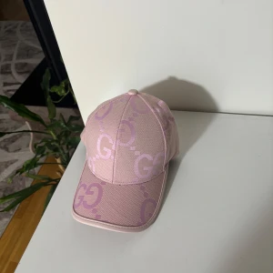 Rosa keps från Gucci - Snygg rosa keps från Gucci med deras ikoniska GG-mönster. Kepsen har en justerbar rem baktill för perfekt passform. Perfekt för att ge din outfit en lyxig touch. Denna annons är den riktiga om du ser en annan så är det någon som försöker kopiera av min bild.