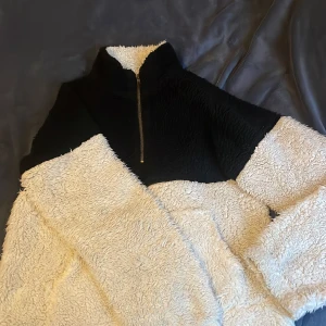 Svart och vit teddyjacka - Mysig teddyjacka i svart och vitt med dragkedja framtill. Perfekt för kyliga dagar med sin fluffiga och varma design. Jackan har långa ärmar och en hög krage för extra värme. är i storlek M men litenn i storlek så passar s/xs