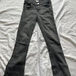 Grå bootcut jeans från Gina Tricot - Snygga grå bootcut jeans från Gina Tricot. De har en klassisk femficksdesign och är perfekta för en avslappnad stil. Jeansen har en knapp och dragkedja framtill. Jeansen har några slitningar/ tecken på användning. Har fler bilder jag skickar privat.