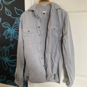 Grå skjorta från Dressman  - Snygg grå skjorta från Dressman  i slim fit. Skjortan har långa ärmar och knappar framtill samt två bröstfickor med knappstängning. Perfekt för en stilren look. 