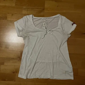Vit t-shirt från Odd Molly - Säljer en vit t-shirt från Odd Molly med knytning framtill och en liten broderad detalj på ärmen. T-shirten har en rund hals och korta ärmar. Perfekt för en avslappnad stil. 