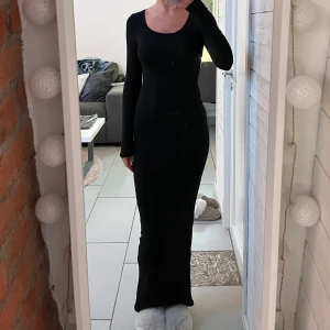 Svart långklänning - Elegant svart långklänning med långärmad design. Klänningen har en tight passform som framhäver figuren och är perfekt för en stilren look. Den är tillverkad i ett mjukt och bekvämt material.
