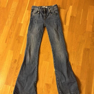 Blå bootcut jeans från Zara - Snygga blå bootcut jeans från Zara med klassisk femficksdesign och knappgylf. Perfekta för en avslappnad stil med en touch av retro. De har en lätt tvättad look som ger dem en cool vibe. Pris kan diskuteras.