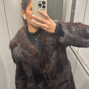 Mörkbrun pälsjacka - Säljer en elegant mörkbrun pälsjacka med lång ärm och klassisk design. Perfekt för att hålla sig varm och stilren under de kallare månaderna. Jackan har en lyxig känsla och passar bra till både vardag och speciella tillfällen. Köpt vintage.