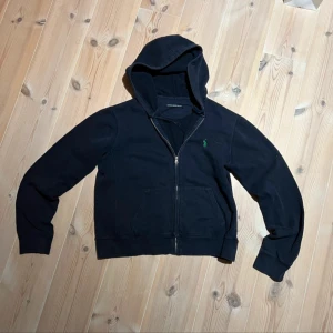 Svart hoodie från Ralph Lauren - Säljer en stilren svart hoodie från Ralph Lauren. Den har en grön logotyp på bröstet och är perfekt för en avslappnad look. Passar bra till både jeans och joggers. Passar nån mellan 159-167cm.