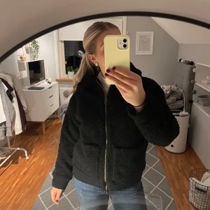 Svart teddyjacka - Mysig svart teddyjacka med dragkedja framtill. Jackan har en normal passform och är perfekt för kyligare dagar. Den har långa ärmar och en hög krage för extra värme. Jackan är jättefin och gosig. 