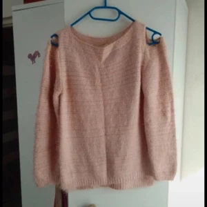 Rosa stickad tröja med cut-out detaljer - Mysig rosa stickad tröja med unika cut-out detaljer vid axlarna. Perfekt för kyliga dagar när du vill ha något både bekvämt och stilfullt. Tröjan har långa ärmar och en rund halsringning.