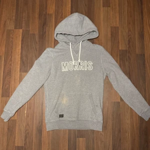 Grå hoodie från Morris - Säljer en stilren grå hoodie från Morris med vit text på bröstet. Passar för dig som är i storlek S, färg fläck på tröjan som syns på bild som går att ta bort.