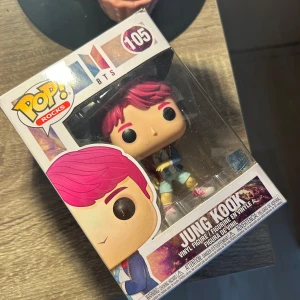 Jung Kook Pop! Rocks figur från BTS - Säljer en Pop! Rocks vinylfigur av Jung Kook från BTS. Figuren har rosa hår och bär en röd och blå jacka med shorts och röda sneakers. Perfekt för samlare och fans av BTS!