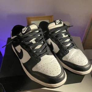 Nike Panda dunk  - Snygga Nike Dunk sneakers i klassisk svart och vit färgkombination. Skorna har en stilren design med snörning och den ikoniska Nike-loggan på sidan. Perfekta för en sportig och trendig look. Kommer med krysskydd, lådan fattas dock. Skorna är i fint skick. 
