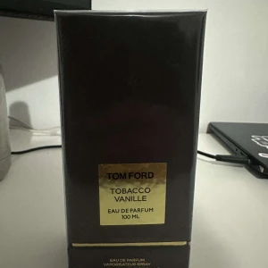 Tom Ford Tobacco Vanille Eau de Parfum 100 ml - Säljer en lyxig parfym från Tom Ford, Tobacco Vanille, i en elegant mörkbrun förpackning med guldtext. Flaskan innehåller 100 ml Eau de Parfum, perfekt för den som älskar varma och kryddiga dofter med inslag av tobak och vanilj.