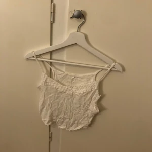 Vit spetsdetaljerad linnetopp - Säljer en söt vit linnetopp med spetsdetaljer. Perfekt för varma sommardagar. Toppen har smala axelband och en luftig passform.