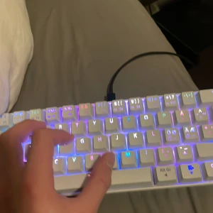 NOS C450 Mini Keyboard Pro RGB - Säljer ett NOS C450 Mini Keyboard Pro RGB med färgglad bakgrundsbelysning. Tangentbordet är kompakt och har en vit design med en orange Escape-tangent. Perfekt för gaming eller arbete med stil.